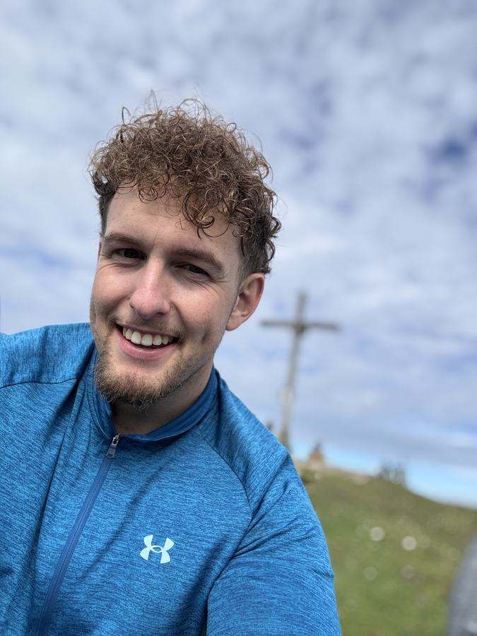 Sebi am Gipfel des Fellhorns, im Hintergrund das Gipfelkreuz und grüne Bergwiesen.